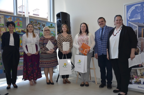 Zdjęcie laureatów konkursu na najlepsze biblioteki powiatu bielskiego przedstawiające uśmiechnięte kobiety na tle rysunków dziecięcych.